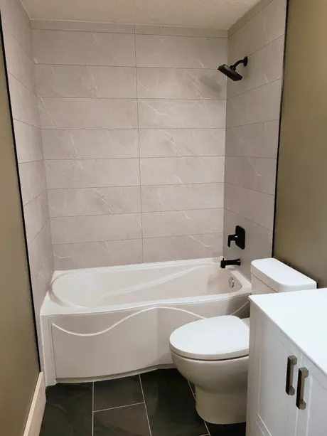 Curved-front bathtub with grey tile-look walls and dark floor, Calgary