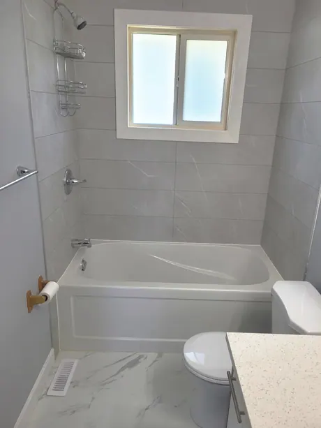 Bathtub with grey marble-look walls, window and quartz sill, Calgary