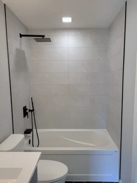 Bathtub with grey tile-look walls beside a white vanity, Calgary